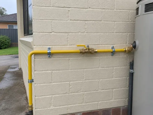 Yellow gas pipe with valve on a cream brick exterior wall beside a water heater in Wetherill Park
