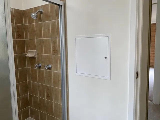 Bathroom wall with a small white access panel beside a tiled shower in Pendle Hill